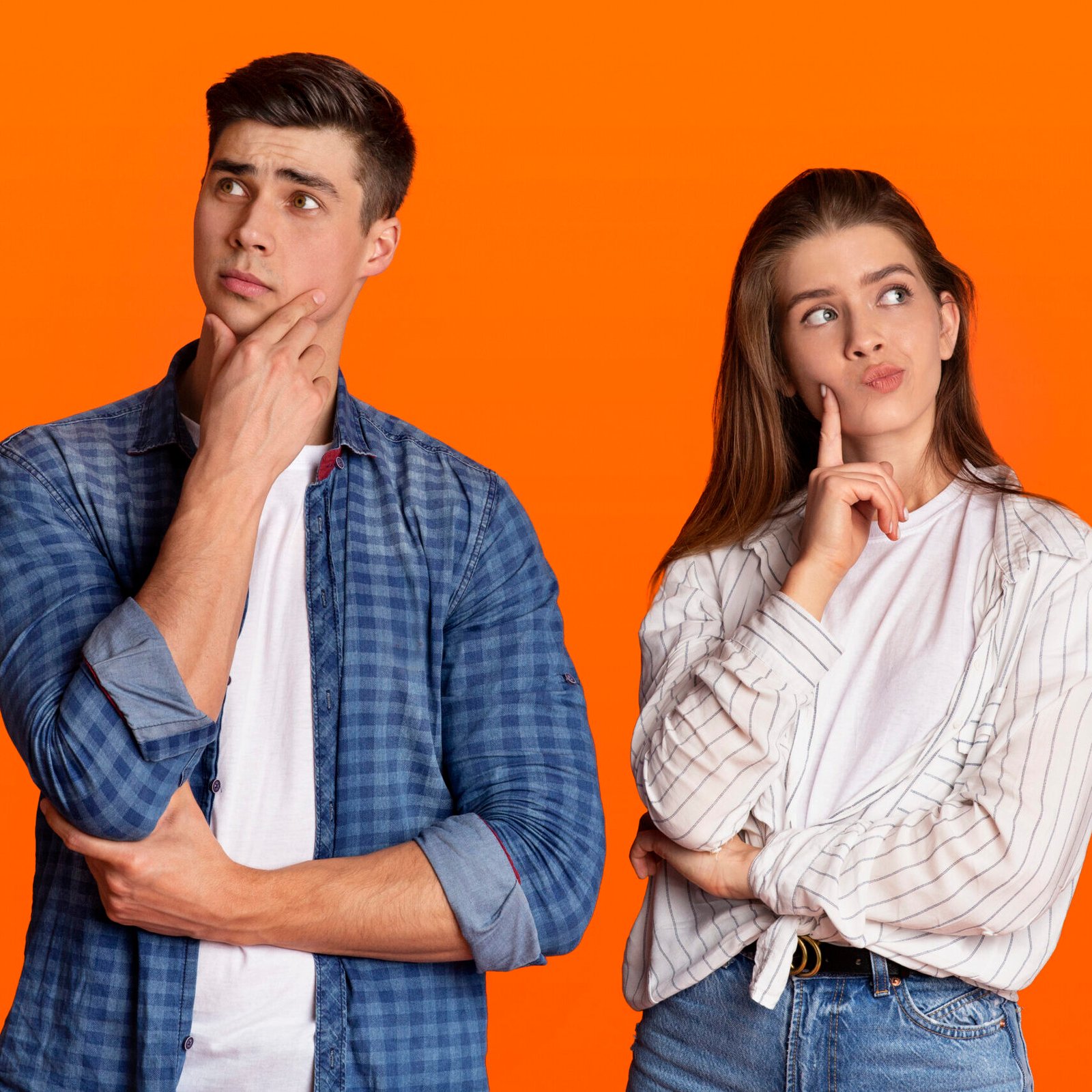 Make decision, new proposal and think about different things. Pensive young couple of students in love press their hands to faces and look at empty space, isolated on orange background, studio shot